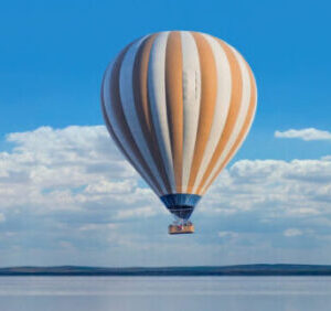 Orange & white striped hot-air balloon over water, blue sky
